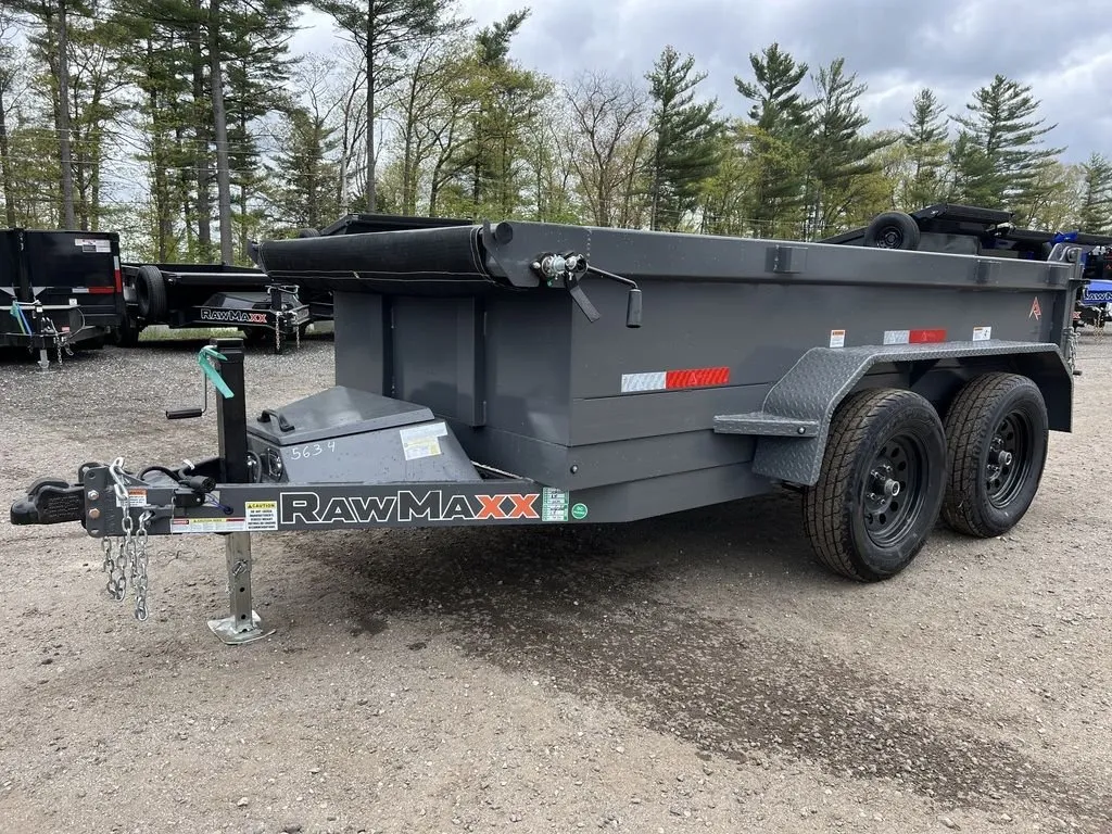 2024 RawMaxx 5x10 dump trailer in charcoal, front three-quarter on gravel with a rolled tarp across the top